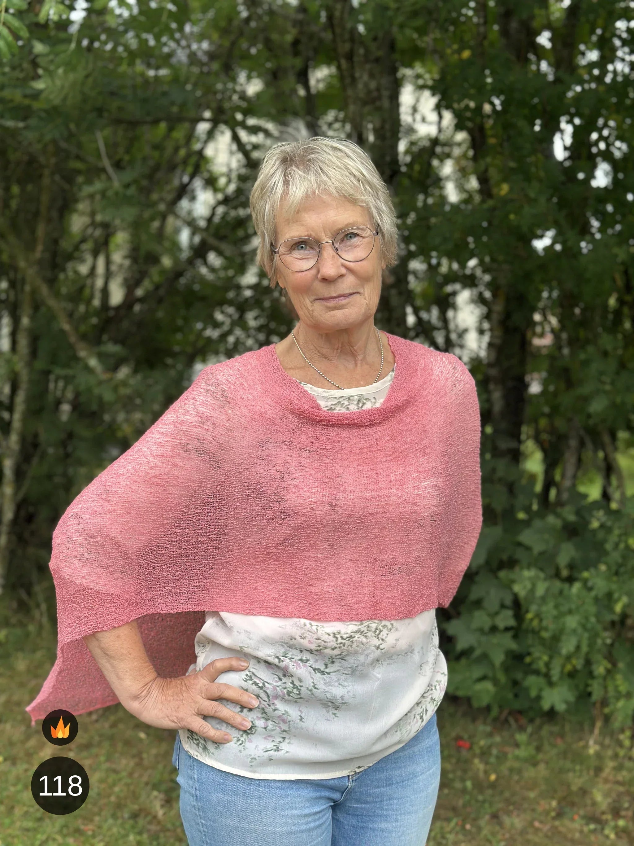 Kvinna bär Ella Cape i färg 118 Gammelrosa, en varm nyans märkt med eldsymbol. Finstickad cape från Ulla Jacobsson Kläder.