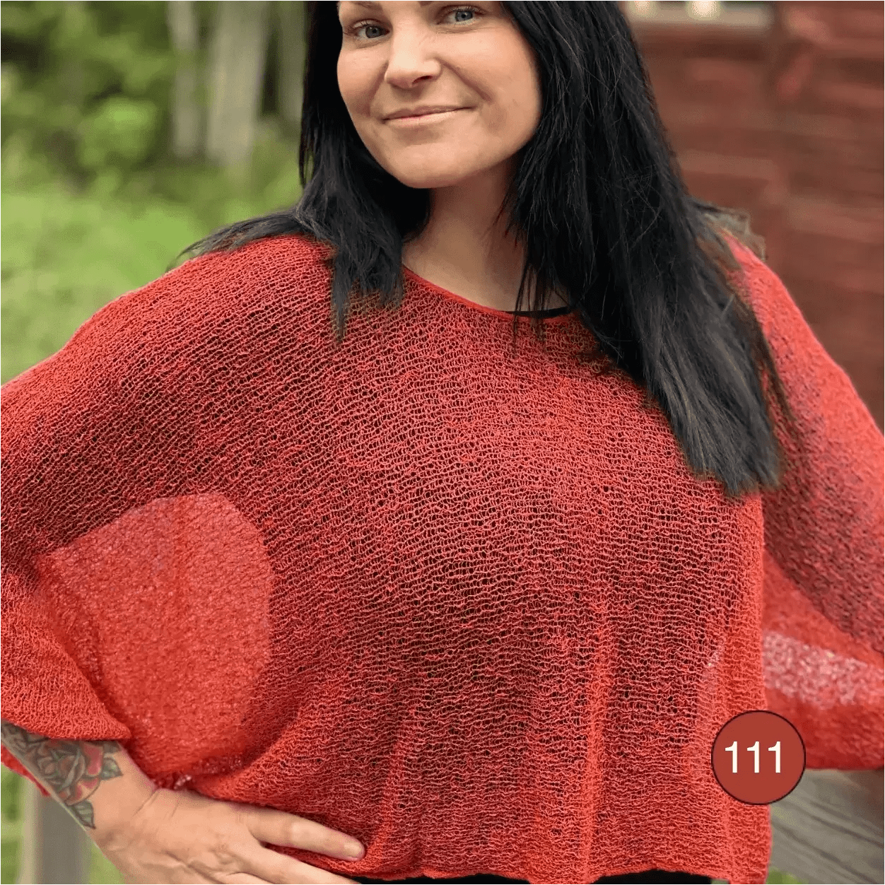 Kvinna i Lebar poncho i färgen Rost nr 111, en varm tegelton, finstickad poncho med vida ärmar som faller mjukt över axlarna. 15 % i augusti hos Ulla Jacobsson Kläder.
