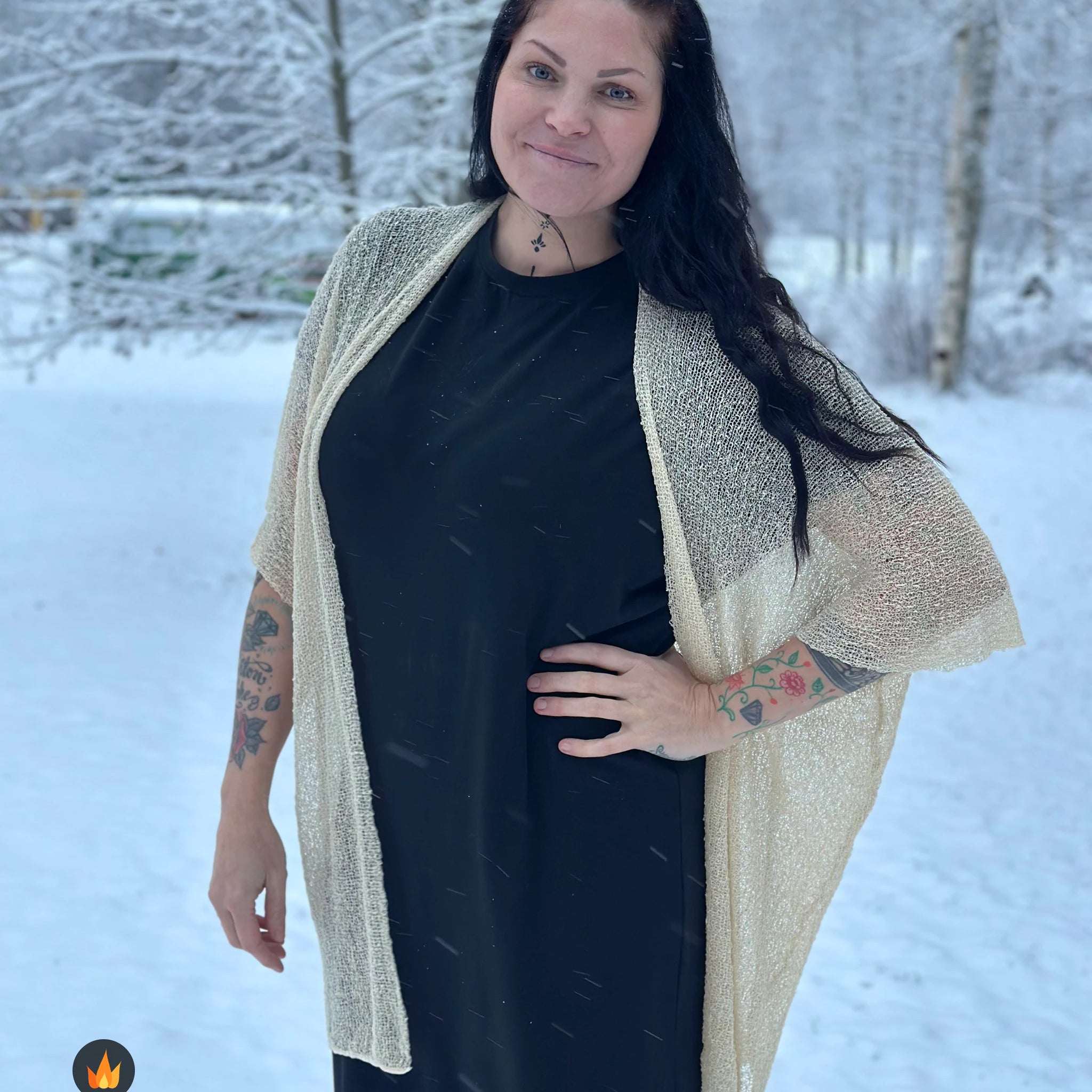 Kvinna bär Biasa Kofta i färg 036 Ljus sand, en varm färg i ljus sandbeige med champagneton, lång finstickad oversized kofta buren öppen, fotad i ett snöigt vinterlandskap. Ulla Jacobsson Kläder.