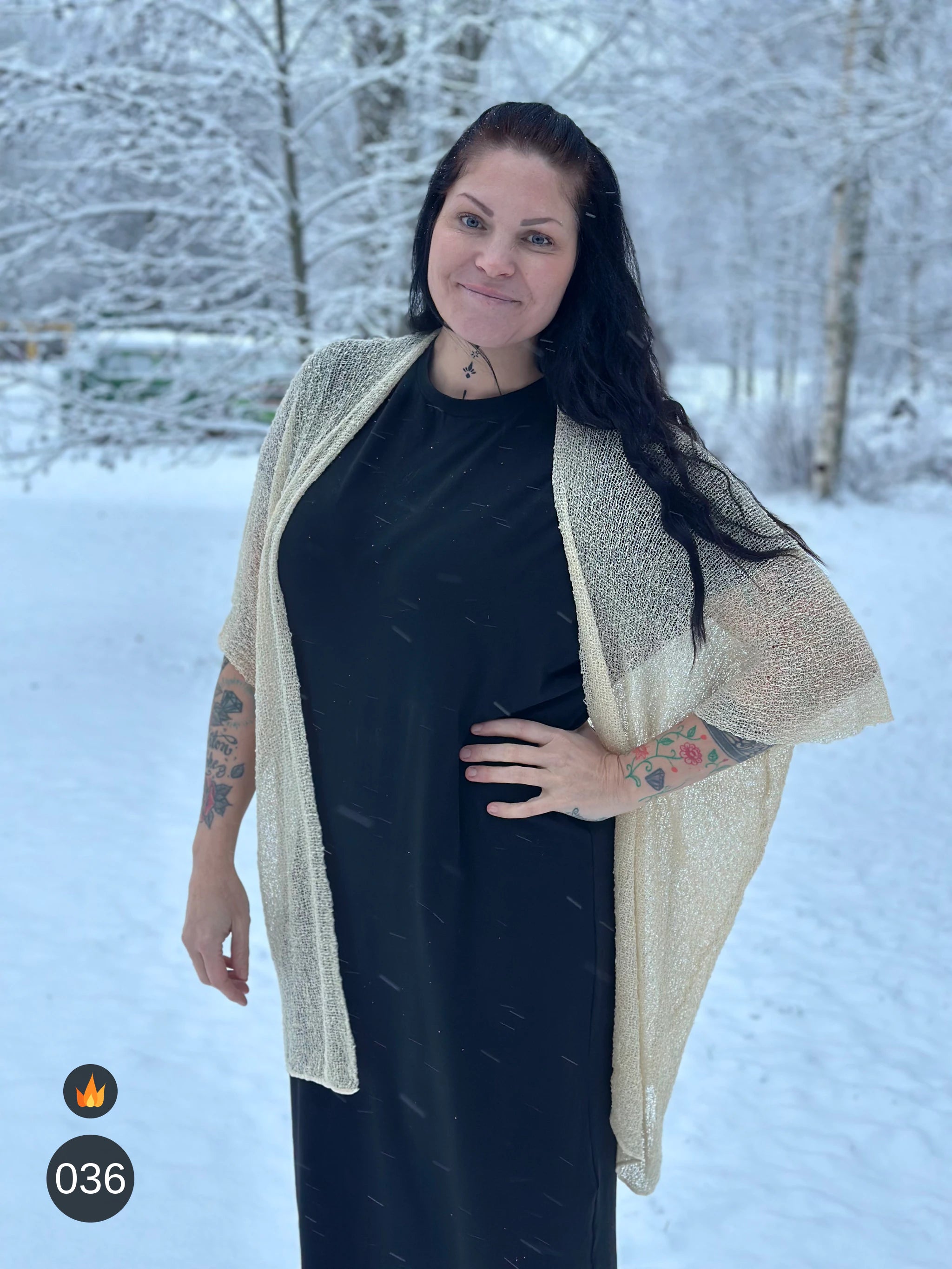 Kvinna bär Biasa Kofta i färg 036 Ljus sand, en varm färg i ljus sandbeige med champagneton, lång finstickad oversized kofta buren öppen, fotad i ett snöigt vinterlandskap. Ulla Jacobsson Kläder.