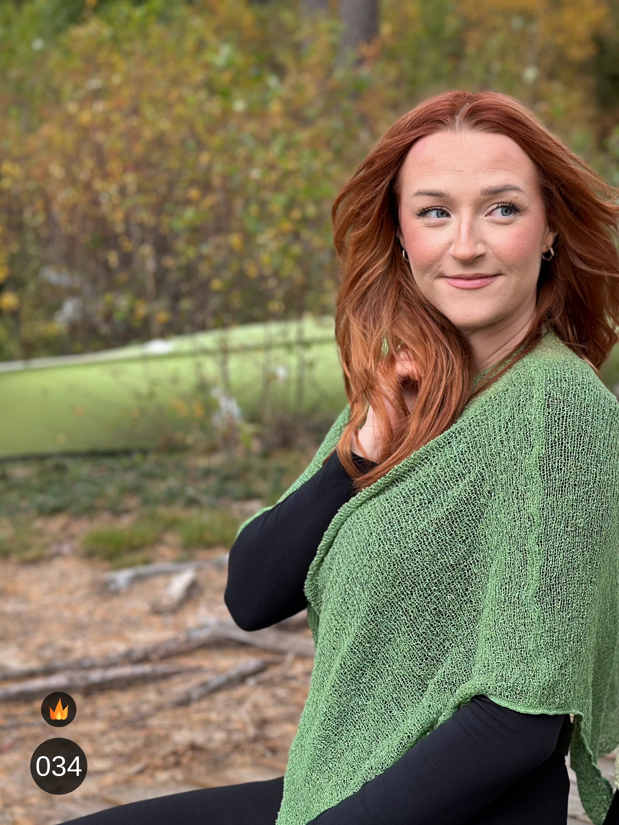 Kvinna bär Ella Cape i färg 034 Ljusgrön, en varm färg i ljus vårgrön, finstickad cape som draperas mjukt över axlarna, fotad utomhus i grönska. Ulla Jacobsson Kläder.