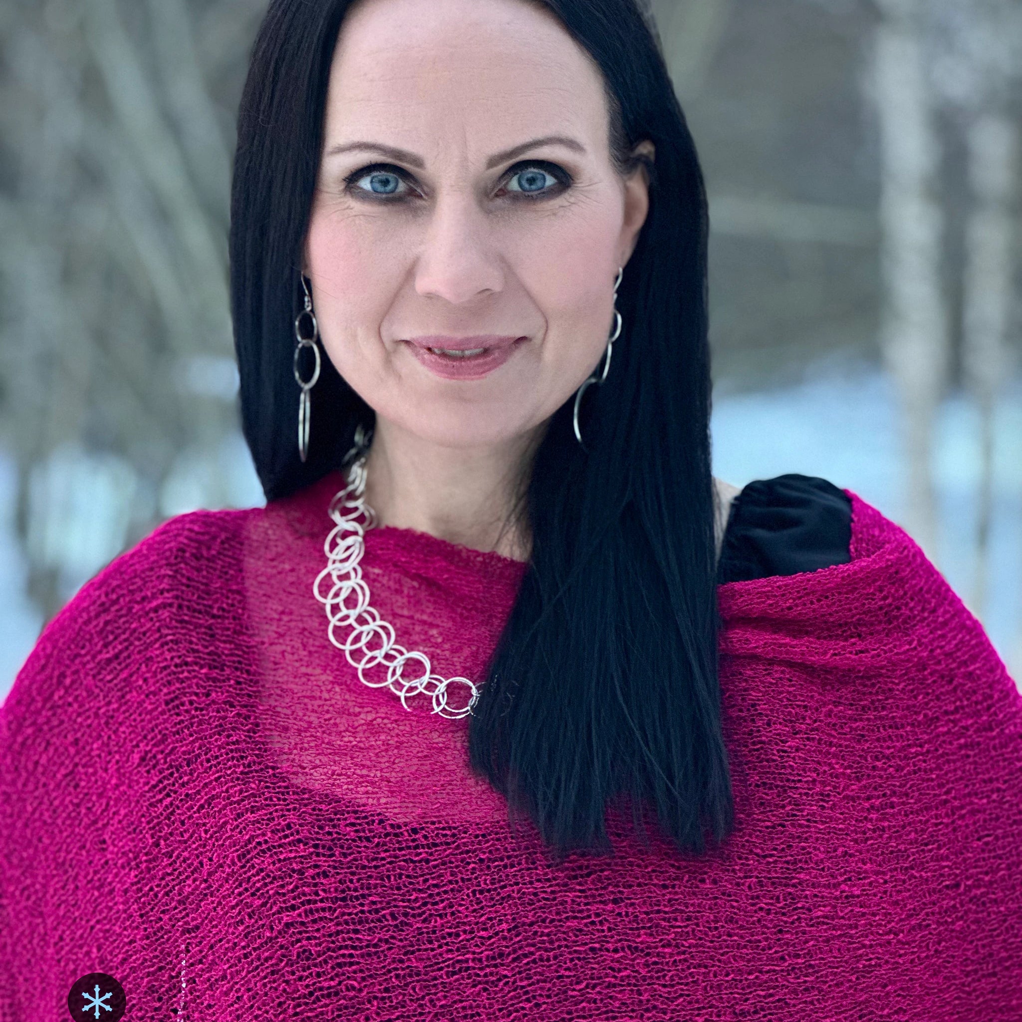 Kvinna bär Ella Cape i färg 104 Fuchsia, en kall färg i intensiv fuchsia, finstickad cape som draperas mjukt över axlarna, fotad i porträtt mot mörk bakgrund. Ulla Jacobsson Kläder.