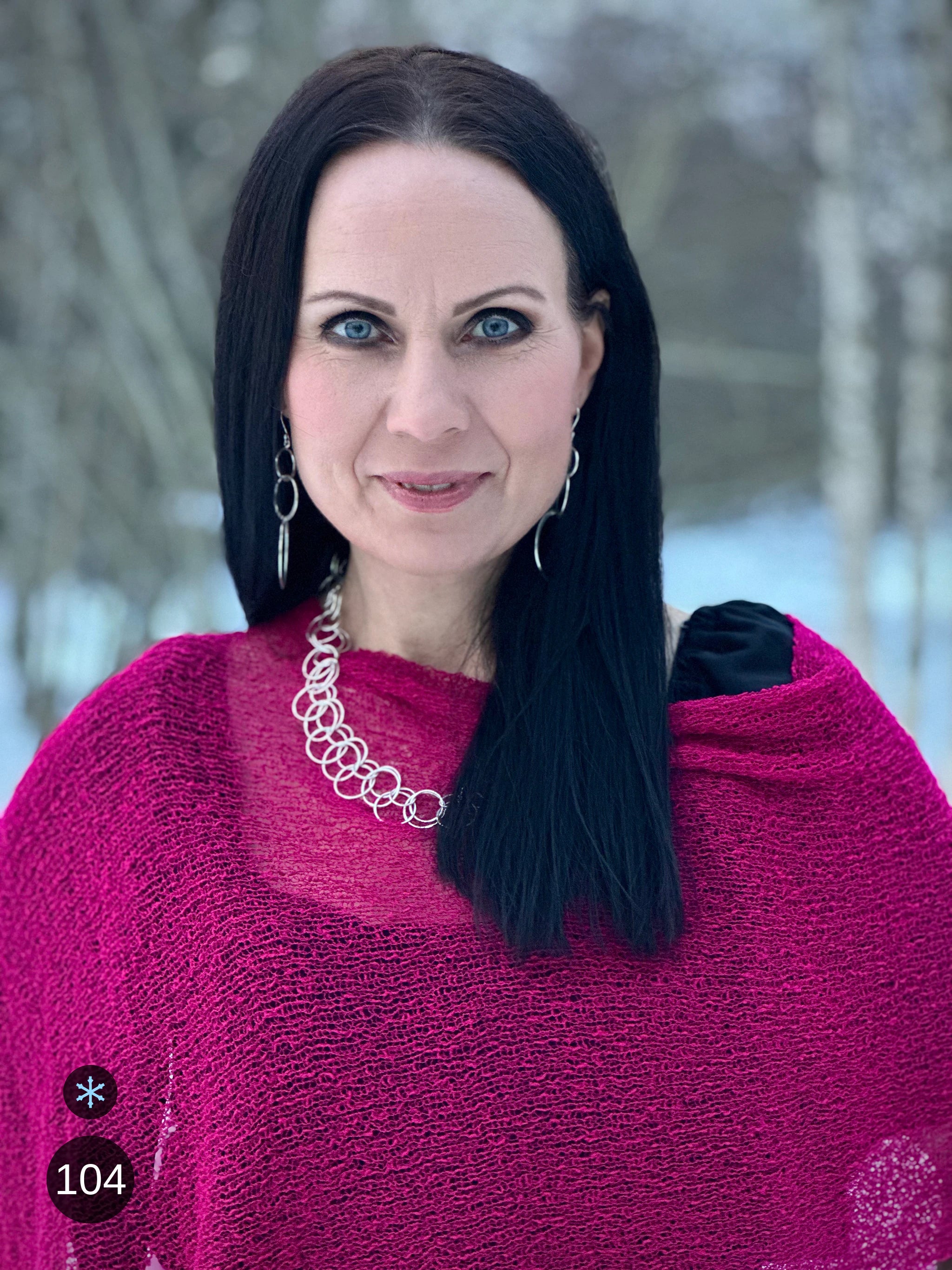 Kvinna bär Ella Cape i färg 104 Fuchsia, en kall färg i intensiv fuchsia, finstickad cape som draperas mjukt över axlarna, fotad i porträtt mot mörk bakgrund. Ulla Jacobsson Kläder.