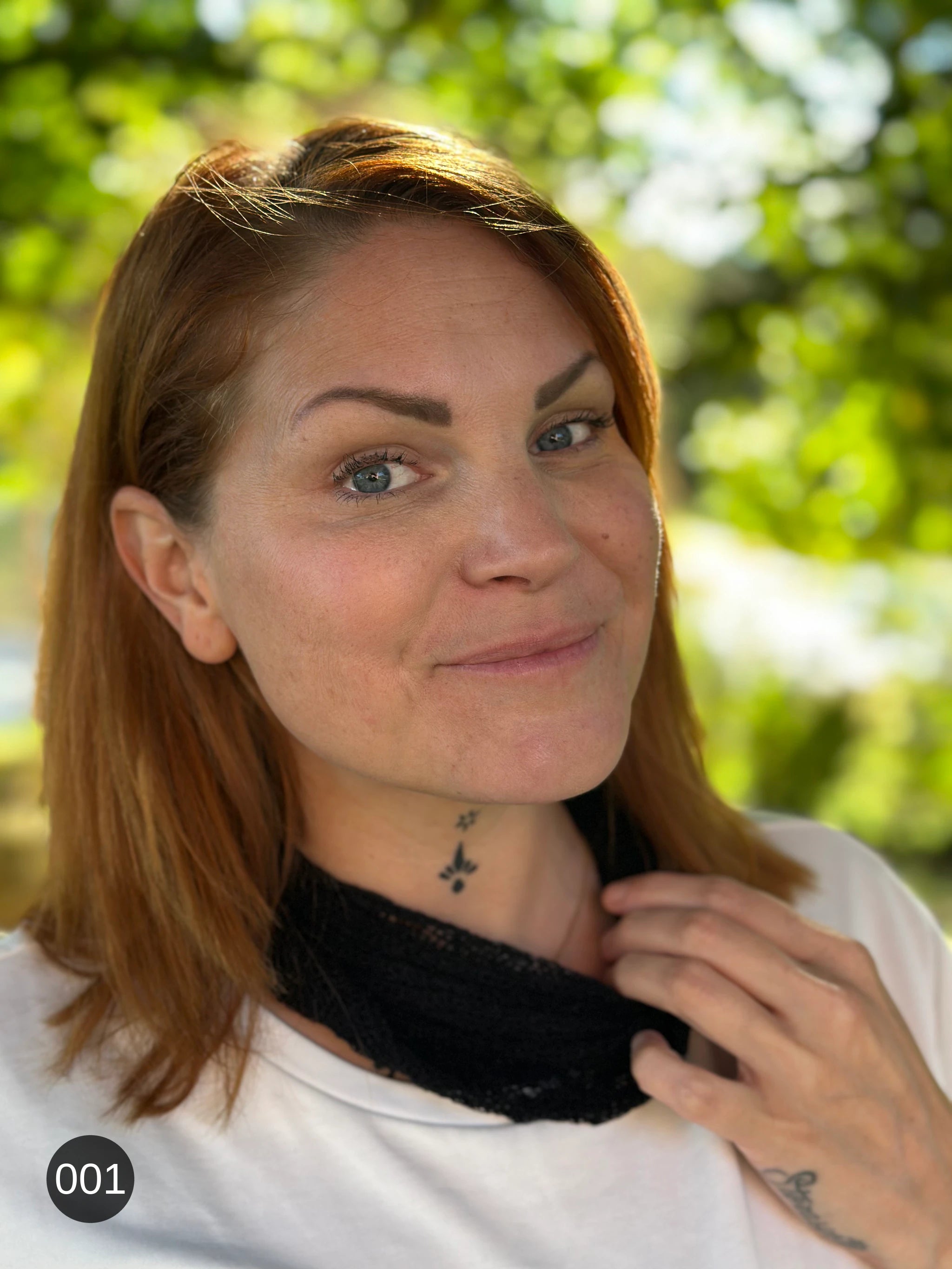 Kvinna bär Eva Tubsjal i färg 001 Svart, en neutral djupsvart med matt yta, liten finstickad tubsjal buren som krage, fotad i höstsol under en lönn. Ulla Jacobsson Kläder.