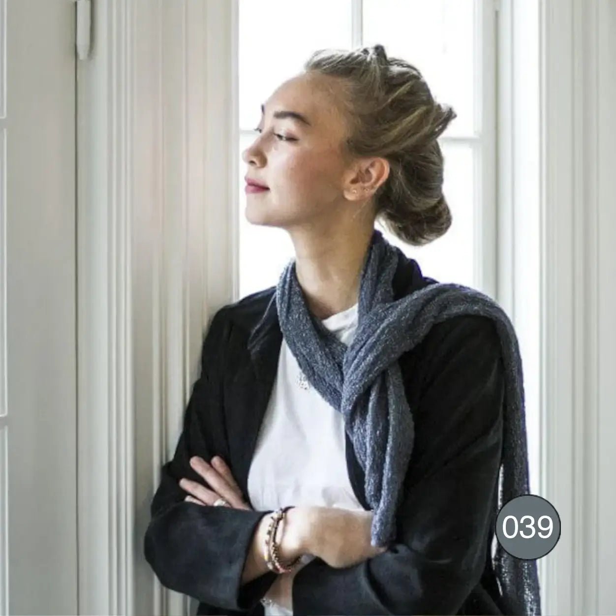 Kvinna med uppsatt hår i svart kavaj, med en Almira sjal i anilin slängd runt halsen; det djupa blågröna garnet faller elegant nedför framsidan. Ulla Jacobsson Kläder