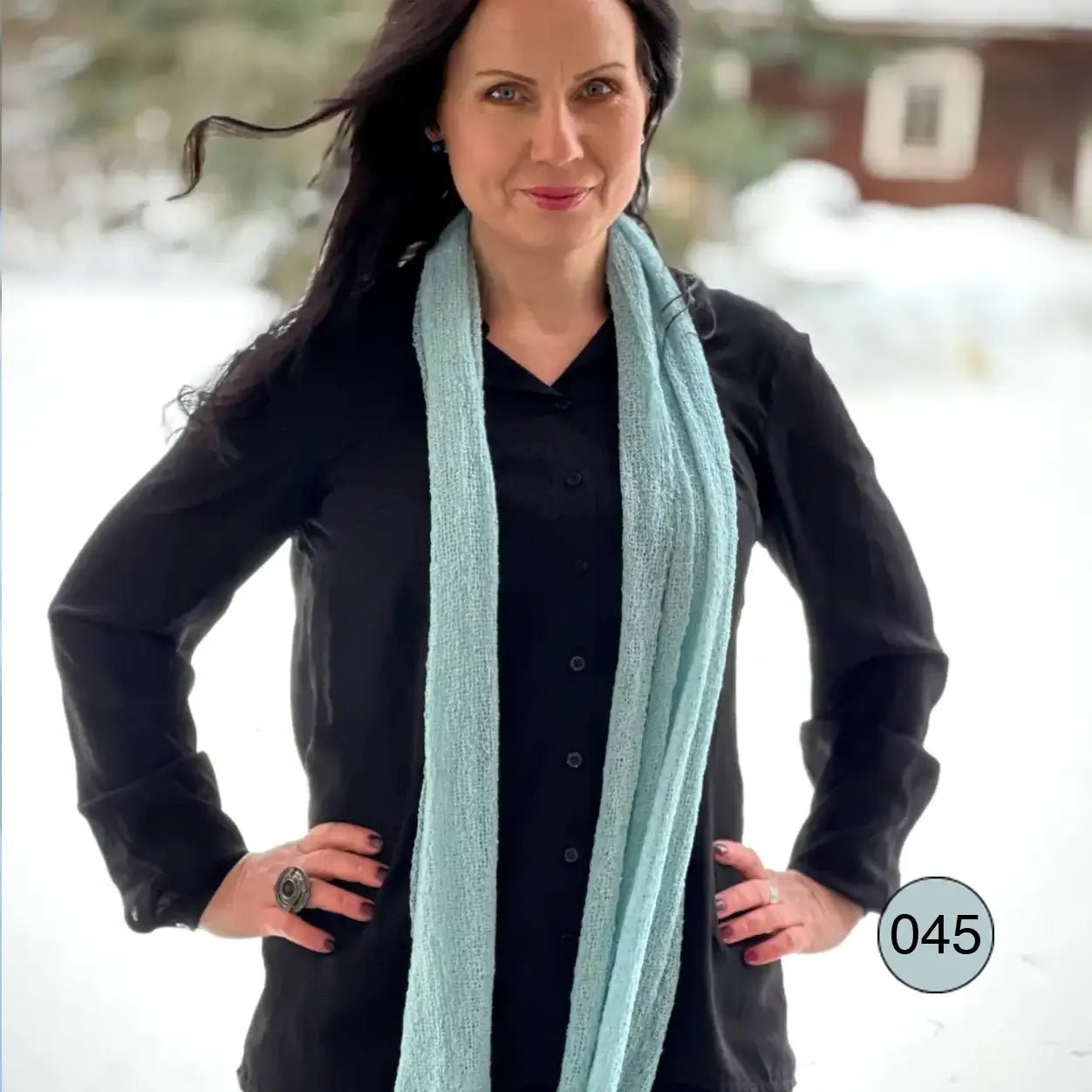 Kvinna i svart topp utomhus med en Almira sjal i himmelblått lagd runt halsen; den finstickade sjalen faller i två mjuka längder nedför bröstet. Ulla Jacobsson Kläder