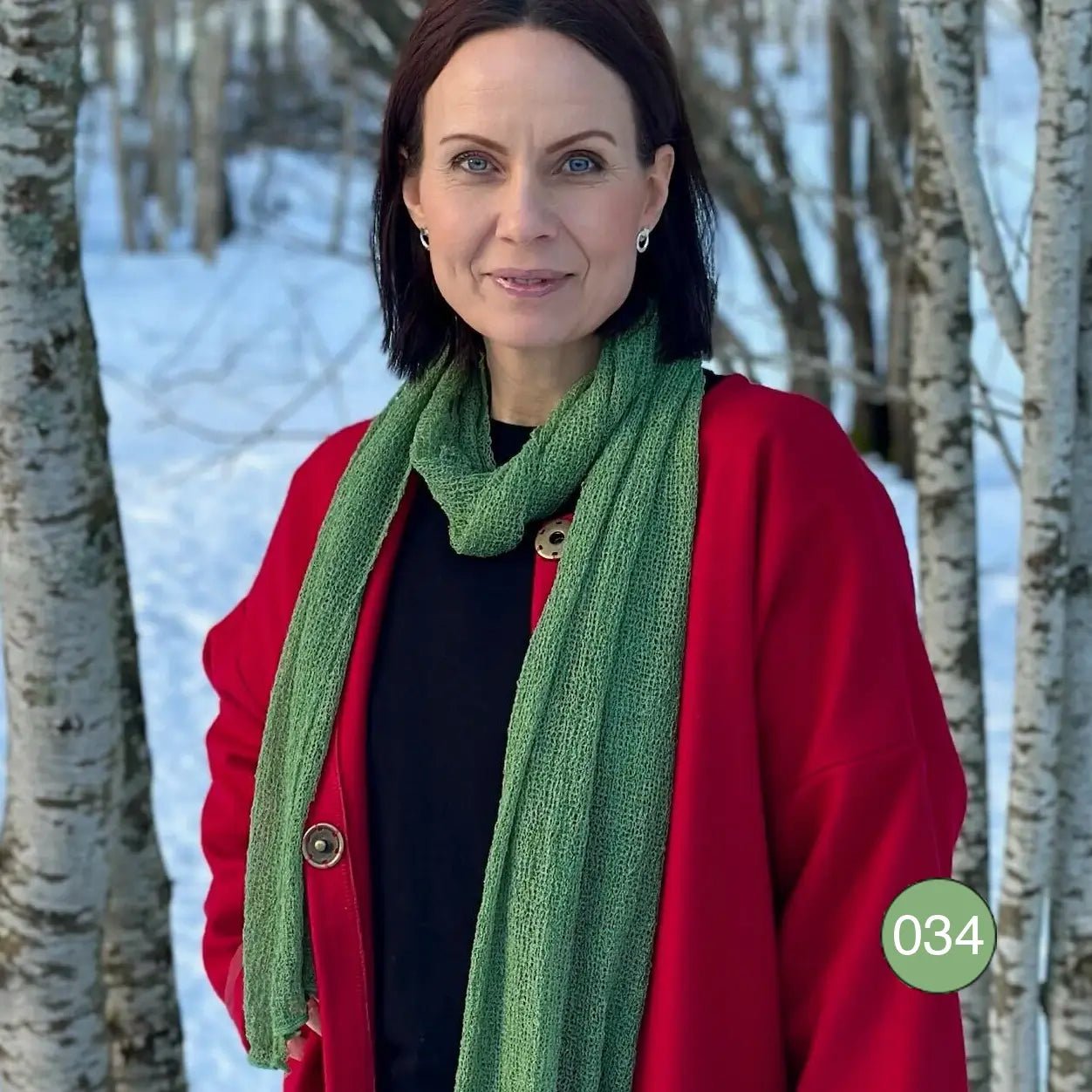 Mörkhårig kvinna utomhus i vinterlandskap med en Almira sjal i ljusgrön ton virad runt halsen över en svart tröja; den långa sjalen faller mjukt nedför bröstet. Ulla Jacobsson Kläder