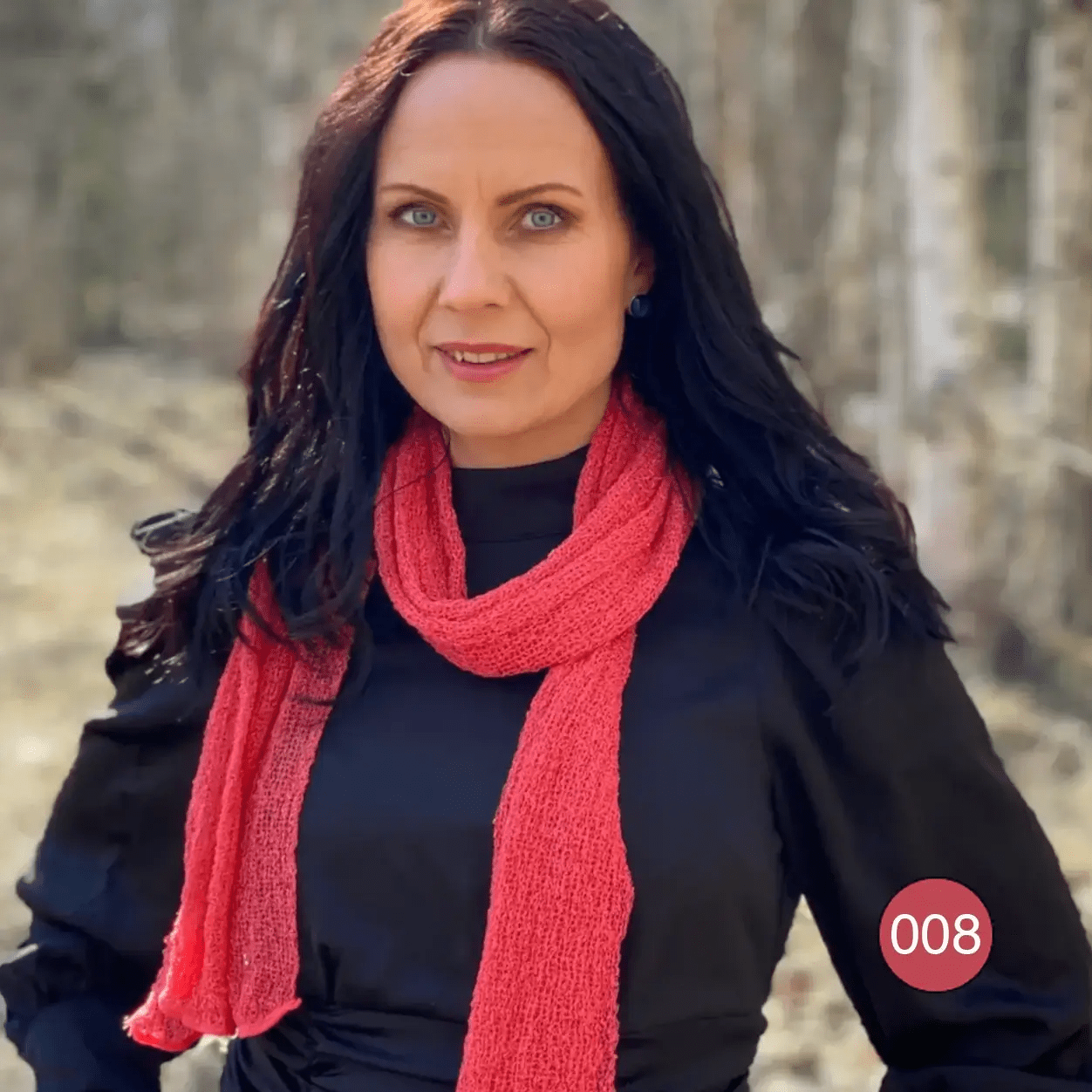 Mörkhårig kvinna i en persikofärgad Almira sjal som hänger löst kring halsen över en mörk topp; det tunna stickade garnet ger ett luftigt, mjukt fall. Ulla Jacobsson Kläder