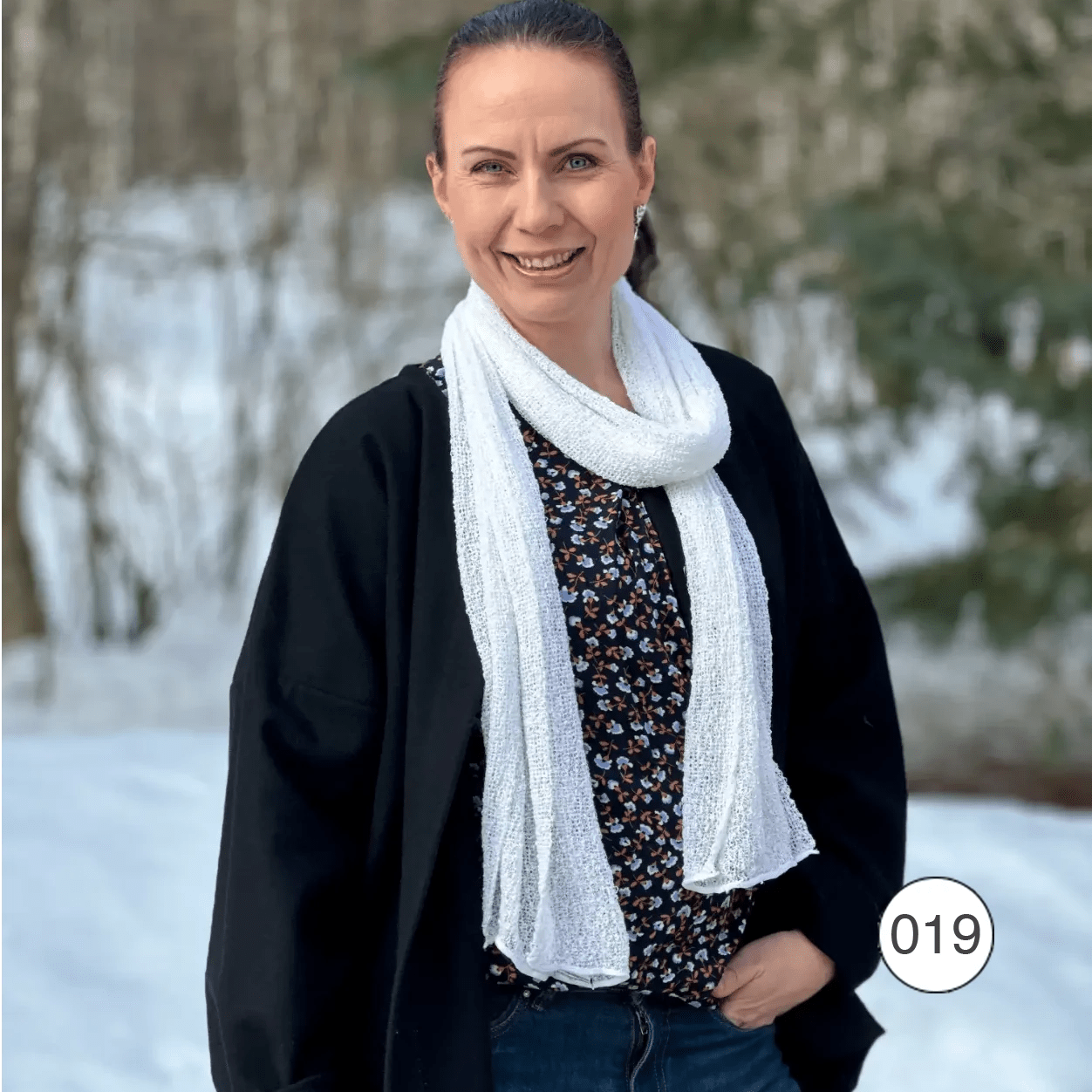 Almira sjal i vitt draperad löst runt halsen på en kvinna över en svart topp inomhus; det tunna stickade garnet ger ett ledigt, mjukt fall. Ulla Jacobsson Kläder