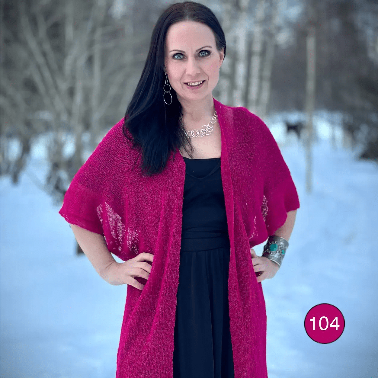 Mörkhårig kvinna mot ljusblå bakgrund som sveper en fuchsia Biasa kofta om sig; det tunna, finstickade garnet lyser starkt cerise över svart. Ulla Jacobsson Kläder