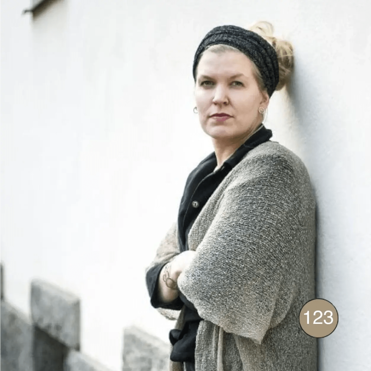 Kvinna med svart sjalett mot en vit vägg i en ljusbeige Biasa kofta; den mjuka, finstickade koftan ligger om axlarna i en ljus gråbeige ton. Ulla Jacobsson Kläder