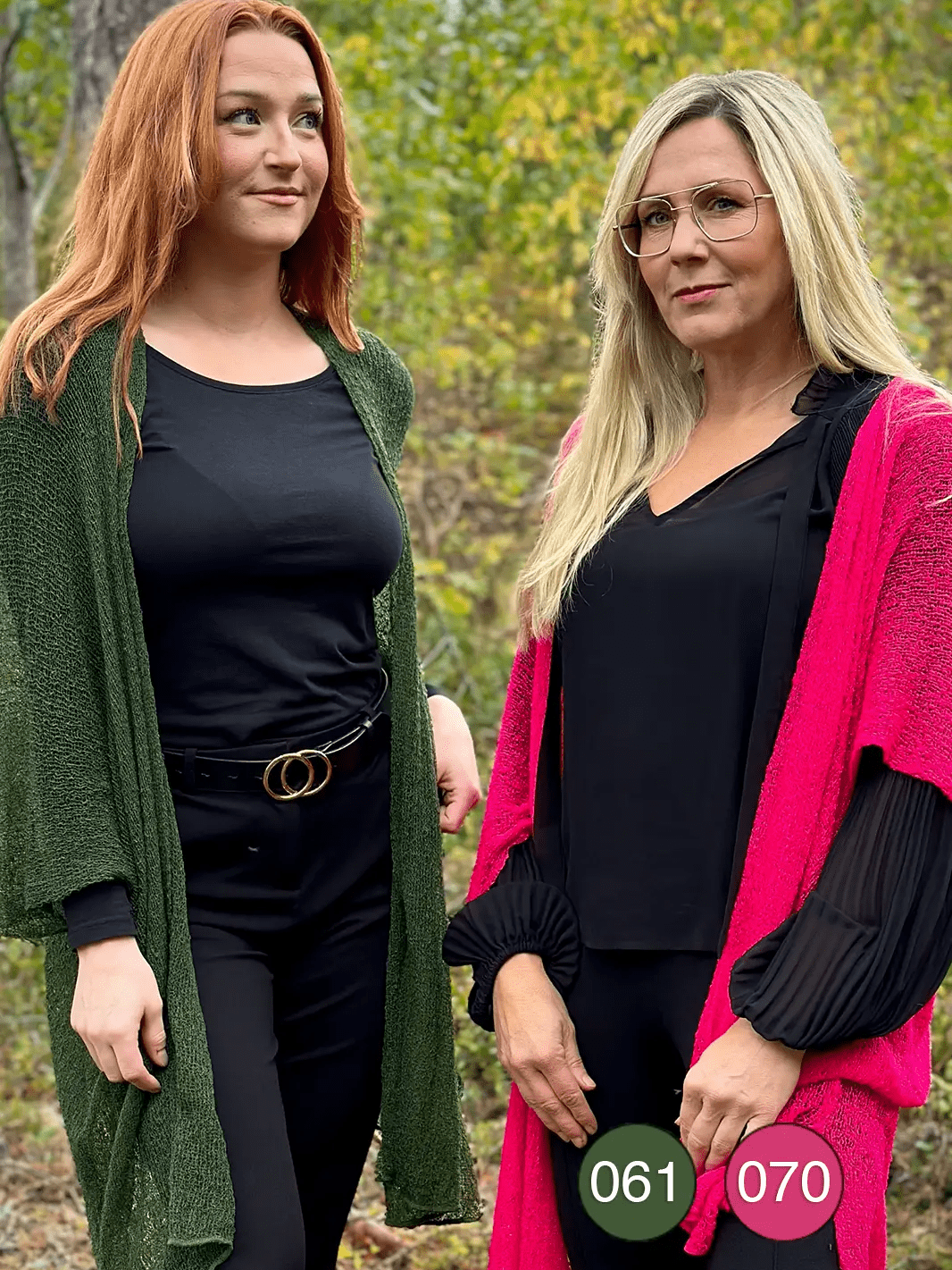 Två kvinnor sida vid sida utomhus, den ena i en mörkgrön och den andra i en neonrosa Biasa kofta – båda långa och finstickade, öppna över svarta plagg och mjukt fallande. Ulla Jacobsson Kläder