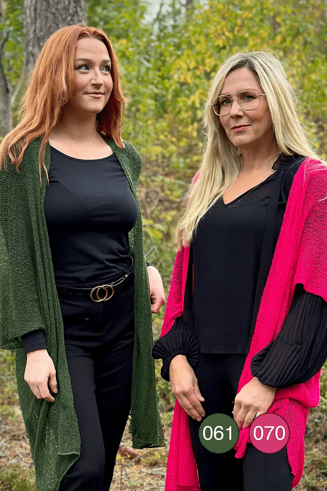 Två kvinnor sida vid sida utomhus, den ena i en mörkgrön och den andra i en neonrosa Biasa kofta – båda långa och finstickade, öppna över svarta plagg och mjukt fallande. Ulla Jacobsson Kläder