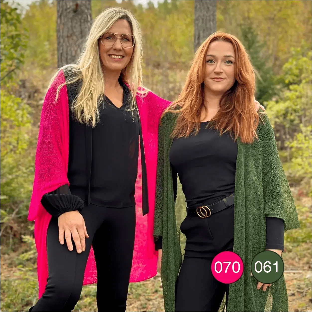 Två kvinnor bredvid varandra, en blond i neonrosa och en rödhårig i mörkgrön Biasa kofta, båda långa och finstickade, öppna över svarta plagg. Ulla Jacobsson Kläder