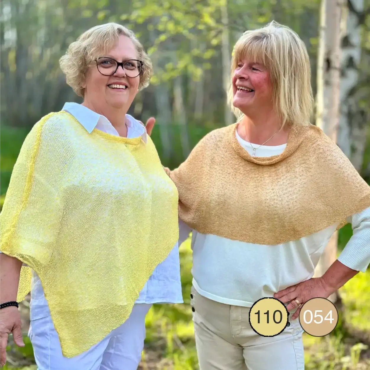 Två kvinnor utomhus, den ena med glasögon i en solgul Ella cape och den andra i en kamelfärgad, med mjuk luftig stickning draperad över axlarna. Ulla Jacobsson Kläder