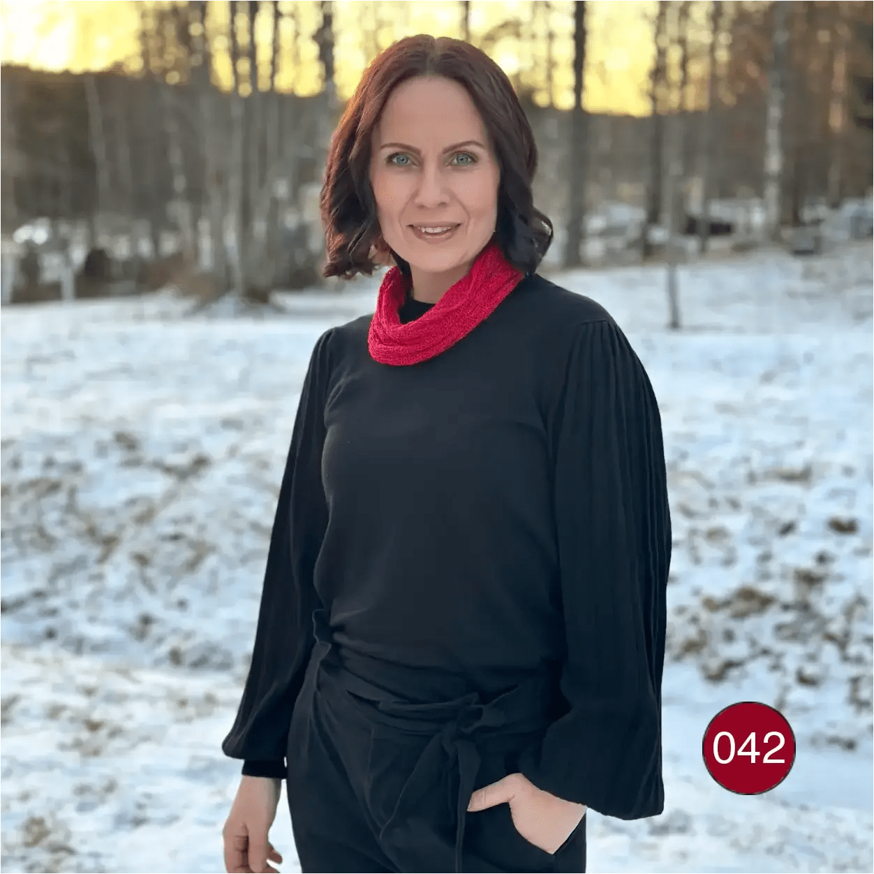 Mörkhårig kvinna utomhus i vinterljus med en röd Eva tubsjal runt halsen över en svart tröja. Ulla Jacobsson Kläder