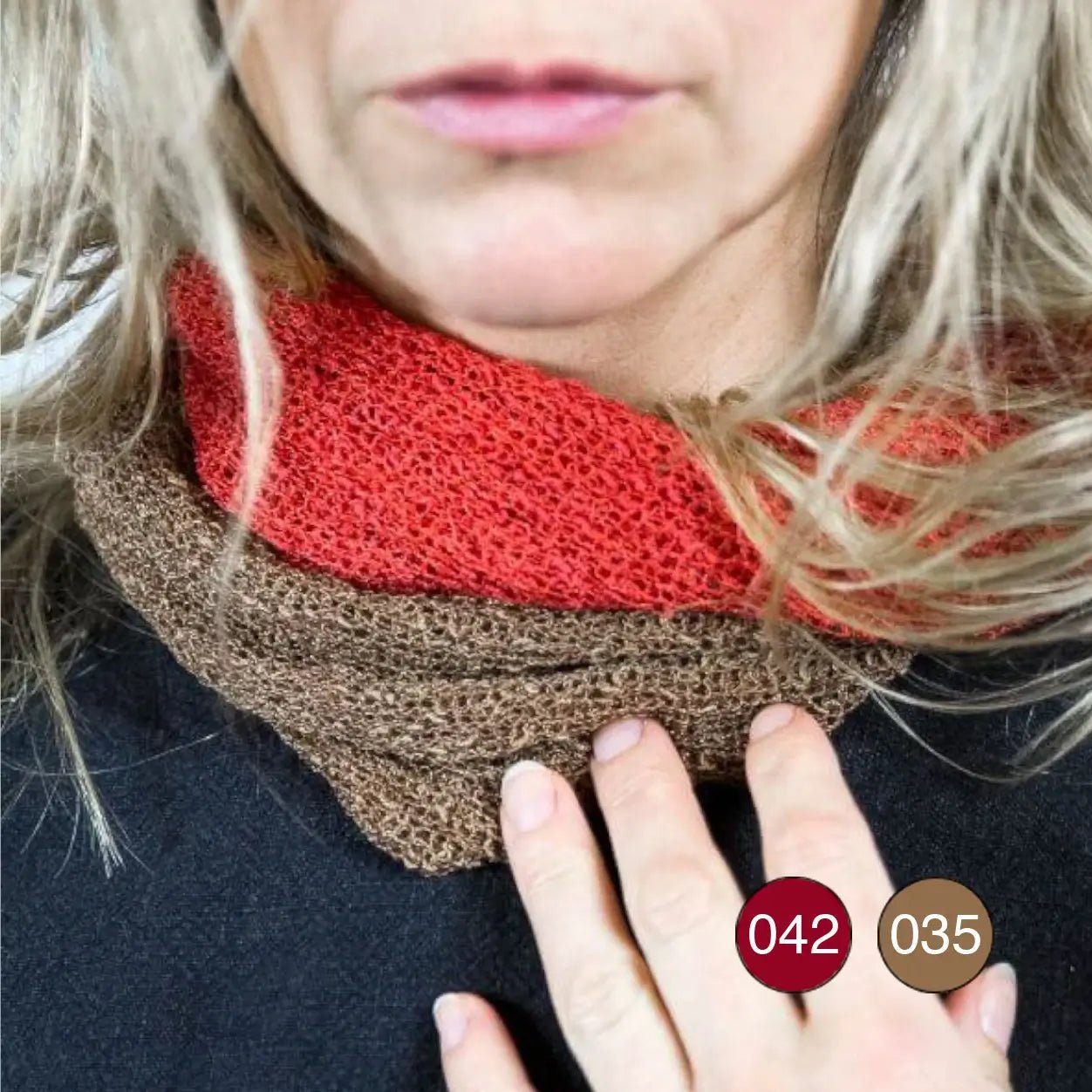 Närbild på en kvinna med vinden i håret som bär två Eva tubsjalar lagrade runt halsen – en röd och en i bärnsten – så att de finstickade tonerna möts mjukt. Ulla Jacobsson Kläder