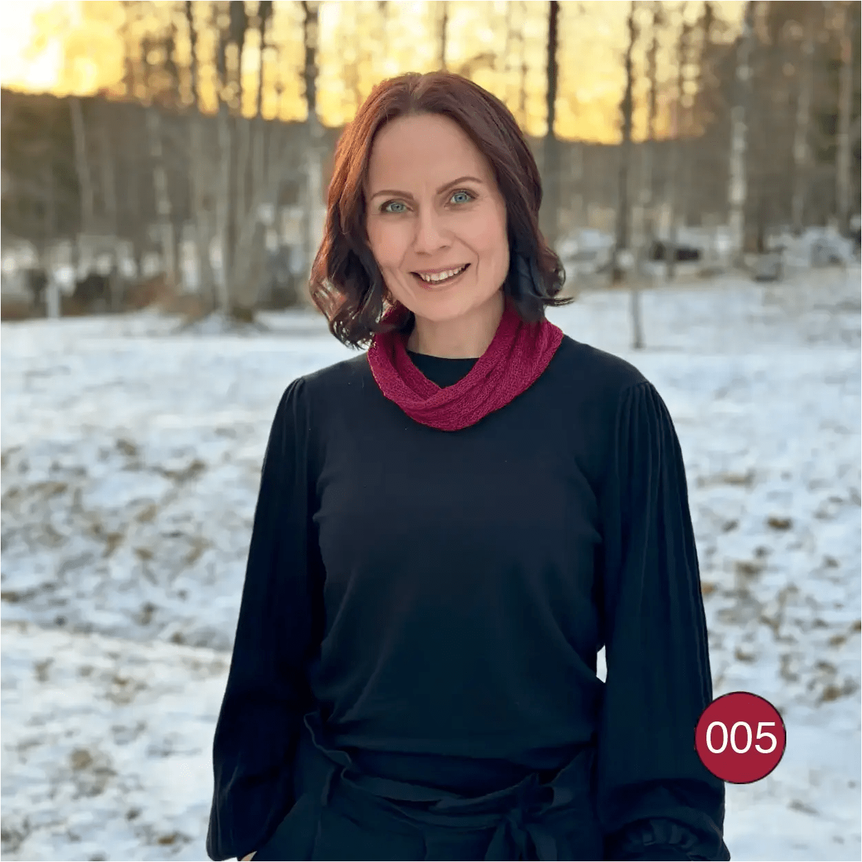 Mörkhårig kvinna utomhus i vintermiljö med en vinröd Eva tubsjal runt halsen som värmer över en svart tröja. Ulla Jacobsson Kläder