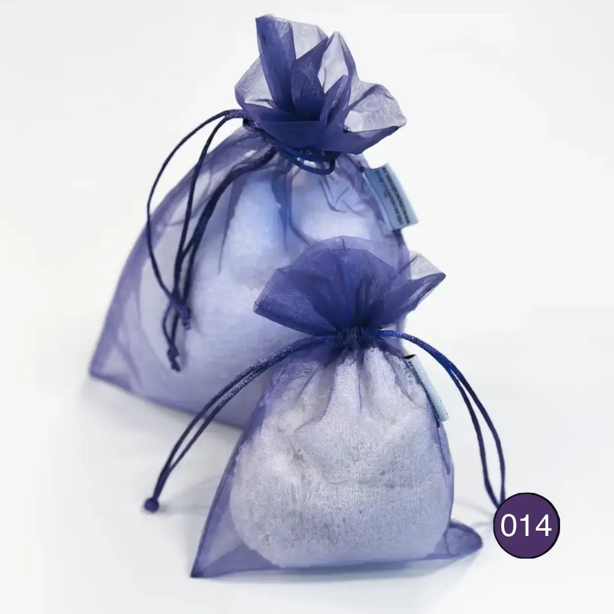 Kaksi tummanviolettia organzaista säilytyspussia eri kokoa, täytettyinä vaalealla ohutneulotulla vaatteella valkoisella taustalla. Läpikuultava organza suojaa vaatteen ja suljetaan nyörellä. Ulla Jacobsson Kläder