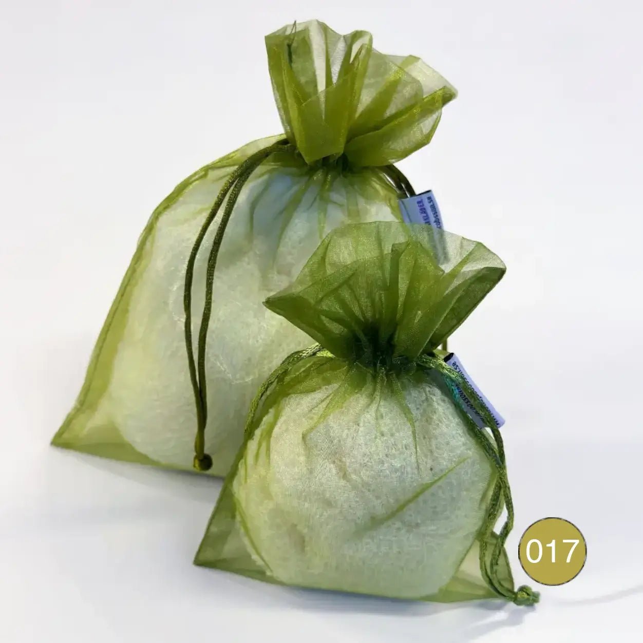 Kaksi oliivinvihreää organzaista säilytyspussia, pieni ja suurempi, täytettyinä vaalealla ohutneulotulla vaatteella valkoisella taustalla. Ohut organza antaa vaatteen hengittää ja suljetaan nyörellä. Ulla Jacobsson Kläder