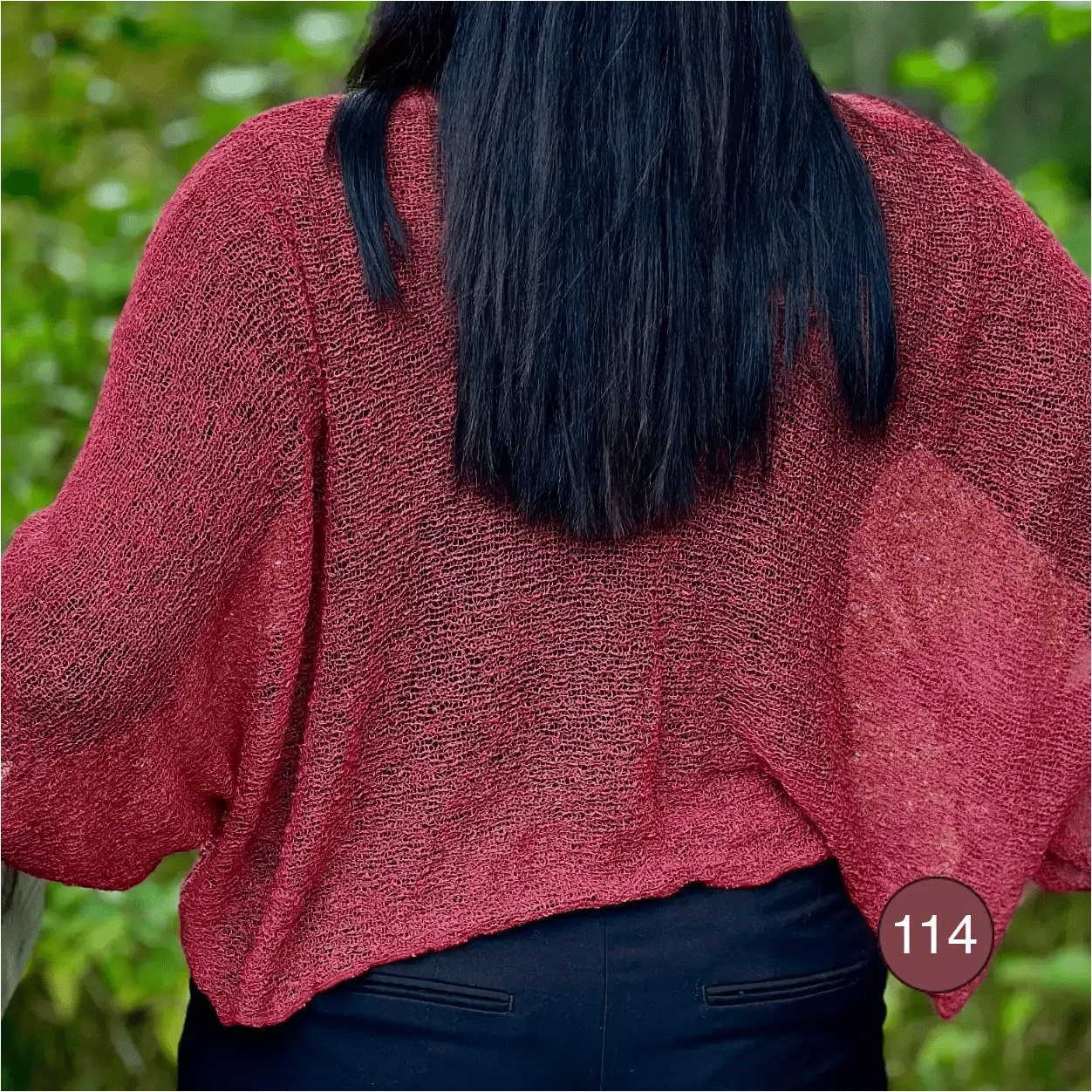 Mörkhårig kvinna fotograferad bakifrån i en Lebar poncho i färgen maroon; det finstickade garnet i mörk vinröd ton draperar mjukt över ryggen och visar det luftiga fallet. Ulla Jacobsson Kläder