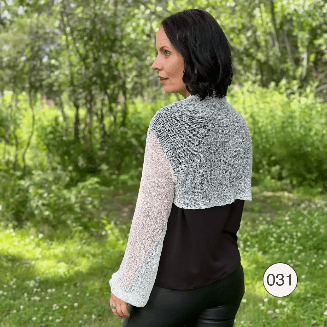 Mörkhårig kvinna sedd bakifrån i en offwhite Liv bolero över svart; det tunna finstickade garnet ramar in axlar och rygg och ger en luftig, ljus avslutning över den mörka underdelen. Ulla Jacobsson Kläder
