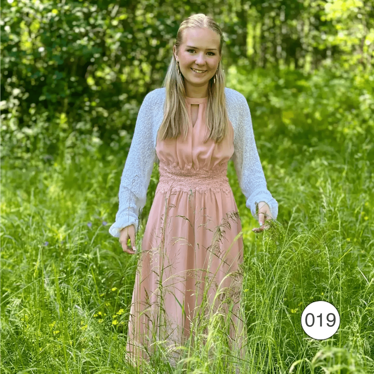 Ljushårig kvinna i björkskog i en vit Liv bolero ovanpå en pudrig rosa klänning; den tunna finstickade boleron lägger ett lätt lager över axlarna och värmer en sval sommardag. Ulla Jacobsson Kläder
