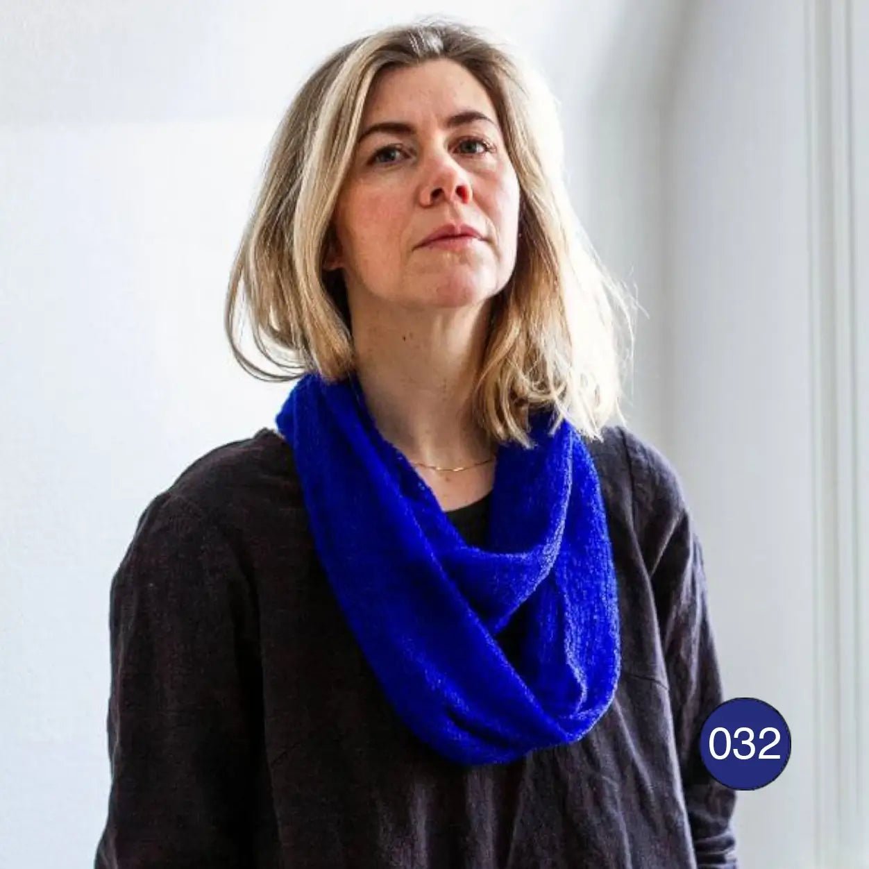 Blond kvinna i svart tröja med en klarblå Sally tubsjal virad runt halsen; det finstickade garnet i klar kobolt ligger mjukt i flera varv. Ulla Jacobsson Kläder