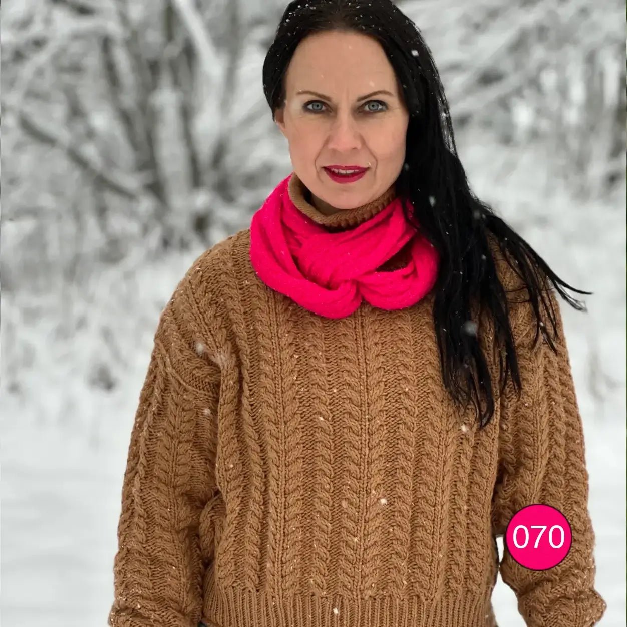 Mörkhårig kvinna i kamelstickad tröja med en neonrosa Sally tubsjal virad runt halsen; den stora finstickade tubsjalen ger en livfull färgklick. Ulla Jacobsson Kläder