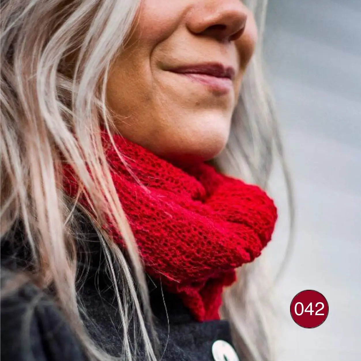 Närbild snett framifrån där en röd Sally tubsjal viras runt halsen mot ljust, vågigt hår; det finstickade garnet syns tunt och mjukt i detalj. Ulla Jacobsson Kläder
